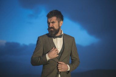 Acımasız sakallı erkek üzerinde bulutlu gökyüzü görünüyor.