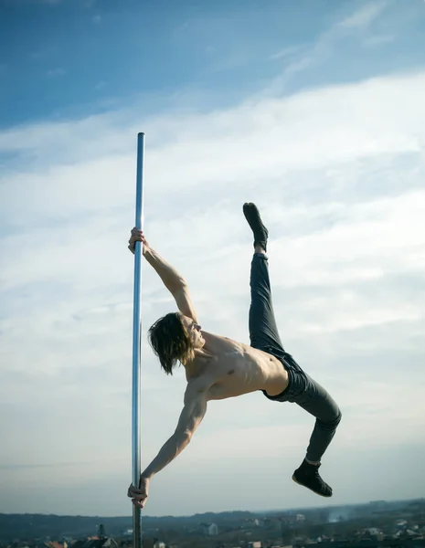 Pole dance sport. pole dance training of young man dancer on blue sky background