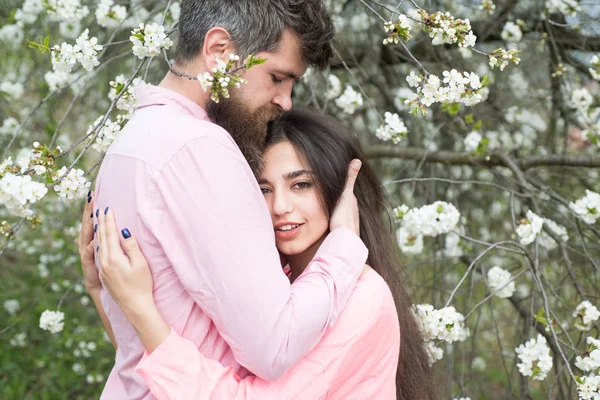 Couple in love spend time in spring garden, branches with flowers on background. Spring date concept. Couple hugs near blooming trees. Man and woman hugs in blooming garden on spring day.