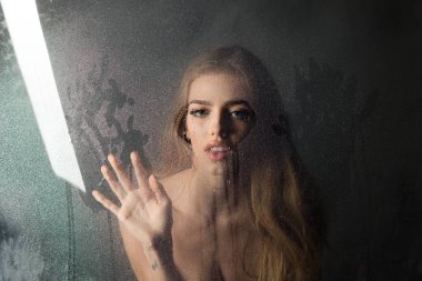 Kalp şeklinde pencere camına yağmur damlaları. Su ile plastik levha arkasındaki seksi kadın bırakır. Kız makyaj ile daha önce su ile pencere bırakır. Duş ve hijyen kaplıca tedavisi. Moda güzellik ve aşk