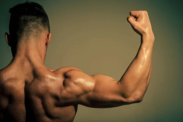 Αθλητισμός και προπόνηση. Αθλητική bodybuilder άνθρωπος σε γκρι φόντο. Δίαιτα και άσκηση, υγιεινό τρόπο ζωής. Προπονητής αθλητής δείχνει δικέφαλου και triceps. — Φωτογραφία Αρχείου