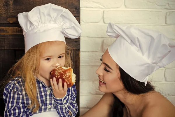 Miúdo feliz a divertir-se. Mulher olhando menino em chapéus chef na cozinha — Fotografia de Stock