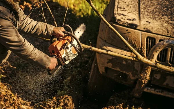 Förbränningsutrustning för hård man. Manliga händer hålla motorsågen och bil täckt med lera — Stockfoto