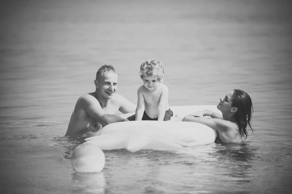 Una coppia innamorata. Famiglia trascorrere del tempo insieme e divertirsi. Carino bambino ragazzo siede sul materasso ad aria ananas a forma di oceano, mare, con i genitori . — Foto Stock