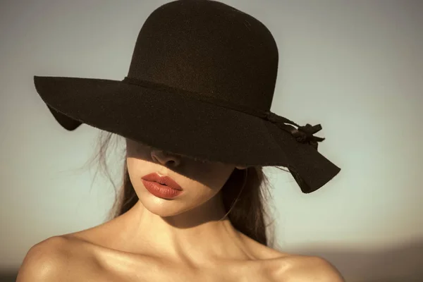 Vrouwelijke gezicht. Problemen van meisjes. Portret van elegante mooie vrouw in een zwarte brede hoed op blauwe hemelachtergrond. — Stockfoto