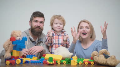 Genç aile inşaat plastik blokları ile oyun oynamak. Aile Oyunları kavramı. Anne ve çocuk mutlu yüzler ile kırmızı tuğla tutun. Baba, anne ve oğlu ışık ahşap arka plan üzerinde oyun odası.