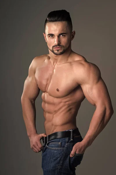 Dieta y fitness. Hombre con cuerpo muscular y torso. Entrenador deportivo con el pecho desnudo en jeans. Atlético culturista hombre sobre fondo gris . — Foto de Stock