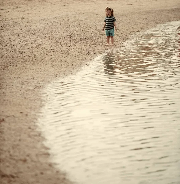 Niños jugando - juego feliz. Bebé niño llorar en la playa del mar en el fondo del paisaje marino — Foto de Stock