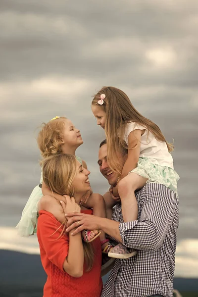 Mutter- und Vatertag. Kinder und Eltern genießen gemeinsam Urlaub. Mädchen sitzen bei bewölktem Himmel auf den Schultern von Mutter und Vater. Sommer, Abenteuer, Entdeckung, Fernweh-Konzept — Stockfoto