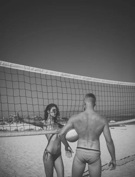 Casal sexy. Jovem casal ativo esportivo ficar perto de rede de voleibol, jogar o jogo no dia de verão. Casal divirta-se jogando vôlei. Mulher e homem em forma, forte, saudável, fazendo esporte na praia. Praia — Fotografia de Stock