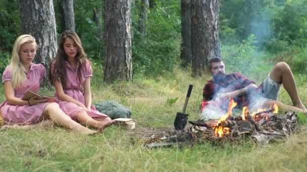 音楽の再生と自然で焚き火を楽しんで幸せな友達。青少年の森で楽しい時を過します。友達の森に座ってキャンプの火のまわりで一周します。. — ストック動画