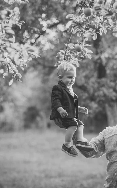 Niños jugando - juego feliz. Niño pequeño sentado en la mano masculina en el jardín de manzanas, confianza — Foto de Stock