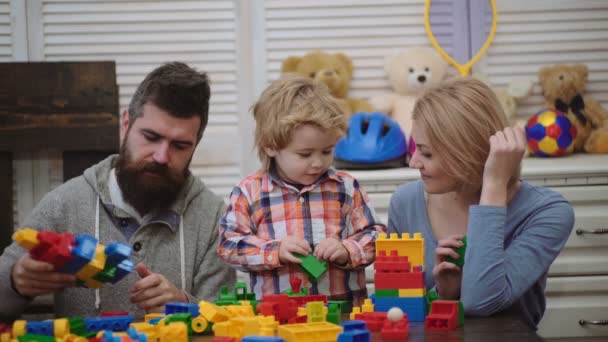 在游戏室的年轻家庭。热爱家庭观念。妈妈, 爸爸和男孩用塑料块制造玩具。父母和儿子微笑, 做砖建筑. — 图库视频影像