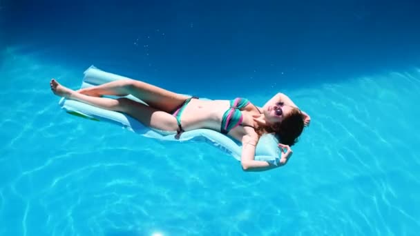 Millennial girl float at pool, festival, hotel, beach, event smiling with sunglasses on during summer. Enjoying suntan. Vacation concept. Top view of slim young woman in bikini on the blue air — Stock Video