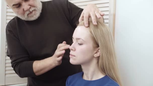 Make-up make-up artiest toepassen op een aantrekkelijke jonge vrouw. Make-up voor het meisje. Jong meisje in de schoonheidssalon. Sexy blond in schoonheidssalon — Stockvideo