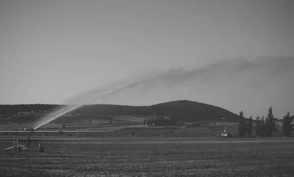 Instalación de aspersores de agua en campo con cielo azul sobre fondo. Sistema de riego en acción en el campo verde. Concepto agricultura y tecnologías — Foto de Stock