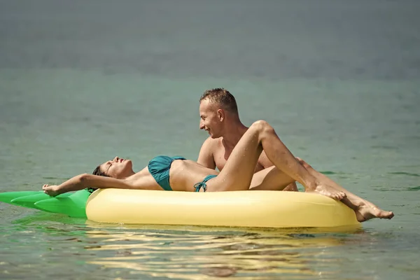 Pareja romántica acostada en la cama. Hombre y mujer en luna de miel, nadar en el colchón en forma de piña en el mar. Feliz pareja joven nadando y riendo en el colchón de aire. Concepto de vacaciones en pareja. Verano — Foto de Stock