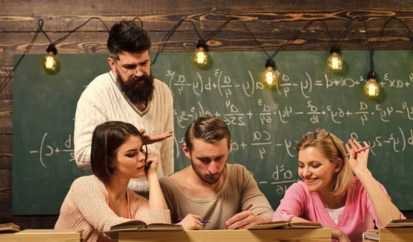 Estudiantes, compañeros de grupo hablando, pidiendo consejo, profesor explica Estudiar el concepto de dificultades. Profesor barbudo, profesor, profesor de enseñanza, pizarra en el fondo —  Fotos de Stock