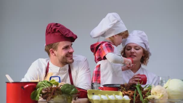 Дети играют - счастливая игра. Милый маленький мальчик и его красивые родители улыбаются во время приготовления пищи на кухне. Молодая семья готовит еду на кухне — стоковое видео