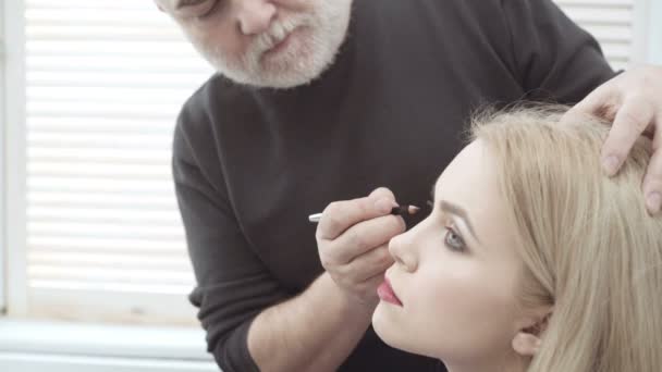 Maquillaje artista aplicar maquillaje a una atractiva mujer joven. Maquillaje para niña. Chica joven en el salón de belleza. Sexy rubia en salón de belleza — Vídeos de Stock