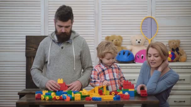 プレイルームの若い家族。家族の概念が大好きです。お母さん、お父さんと男の子のおもちゃでは、プラスチック製のブロックから構築します。両親と息子の笑みを浮かべて、レンガの壁を作る — ストック動画
