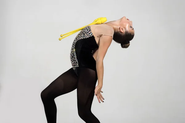 Woman gymnast in black sportswear with yellow mace. Workout of girl on grey background. Gymnastic school and energy. Flexibility in acrobatics and fitness health. Sport and success.