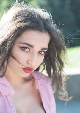 Şehvetli kadın mükemmel makyaj ve açık havada poz shinning uzun esmer saç. Doğal arka plan, kozmetik ve güzellik kavramı üzerinde pembe gömlekli tam kırmızı dudaklar ile çekici kız.