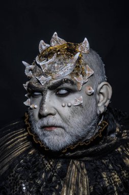 Şeytan siyah zemin üzerine altın yakalı. Adam dikenler veya siğiller ile yüz pırıltılar ile kaplı. Beyaz sakallı komuta sizde canavar gibi giyinmiş. Uzaylı, iblis büyücü makyaj. Fantezi kavramı.