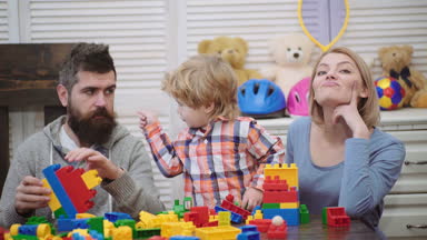 Genç aile oyun odası. Aile kavramı seviyorum. Anne, baba ve çocuk oyuncakları ile dışarı plastik blokları inşa. Anne ve oğlu gülümseyen, tuğla yapılar yapmak