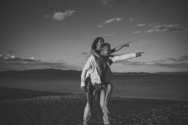 Adam arka, çift tatilde mutlu beyaz elbiseli kadın taşır. Aşık çift aynı yönde işaret plaj üzerinde durmak. Çift eğlenceli ve deniz manzarası arka plan var. Düğün, yeni evli kavramı