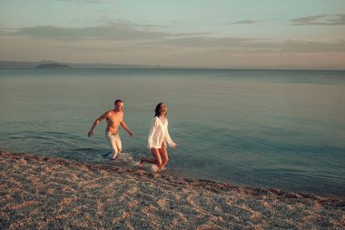 Şehvetli aşk oyunu. İki aşık. İki aşık deniz ya da okyanus plaj su sıçrama içinde çalıştırın. Özgürlük kavramı. Kadın erkek gömlek ve deniz dalgalar halinde çalışan giyer. Erkek ile kadın, oyna yakalar