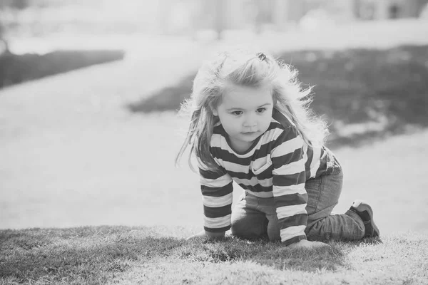 Un enfant heureux qui s'amuse. Garçon aux longs cheveux blonds assis sur l'herbe verte — Photo