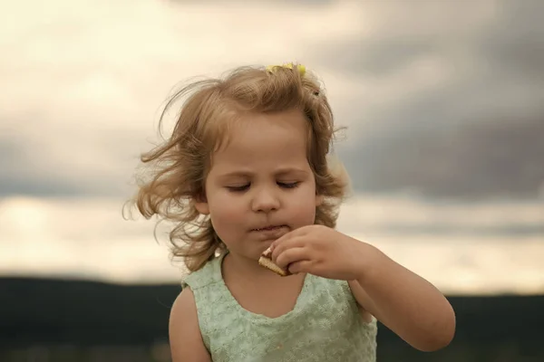 Um retrato de rosto de menina na tua publicidade. Menina criança comer biscoito no dia de verão no céu nublado — Fotografia de Stock