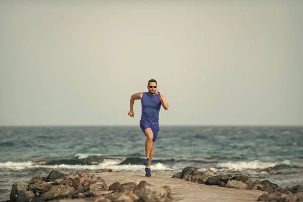 Mens geneest lichaamsverzorging. Loper man loopt op zee strand op blauwe hemel — Stockfoto