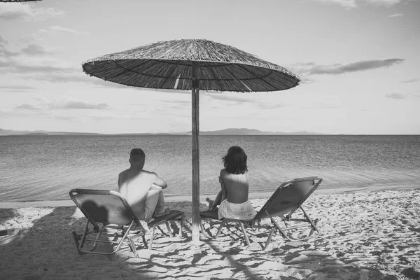 Şehvetli aşk oyunu. İki aşık. Tatil veya balayı Çift. Erkek ve kadın üstsüz deniz, arka görüş üzerinde manzarasının tadını çıkarın. Balayı konsepti. Deniz Resort aşık çift şezlong şemsiye altında oturur — Stok fotoğraf