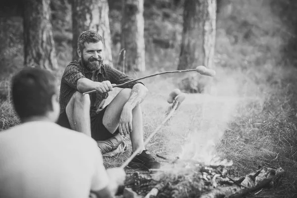 Amis hommes rôtir des saucisses sur des bâtons sur le feu de camp dans la forêt — Photo