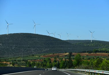 Dağ manzarası yolda. Asfalt yol ve rüzgar türbinleri üzerinde mavi gökyüzü. Yön ve hedef. Alternatif enerji kaynakları. Yaz tatili seyahat ve yolculuk tutkusu