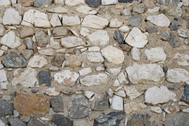 Taş yüzeyi kaba doku. Taşlı zemin üzerine taş duvar. Duvar eski malzeme kayalar. Savunma ve sur kavramı. İnşaat kullan mimari ve tasarım