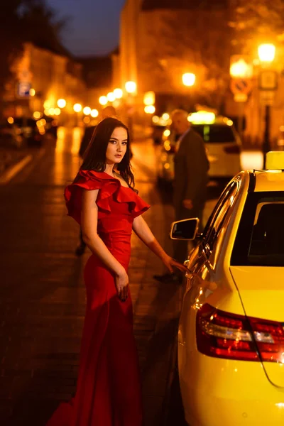 Luxus-Frau im Abendkleid in der Nacht Stadt gehen zum Abschlussball mit dem Taxi. Luxusfrau im roten Kleid wartet auf Taxi. — Stockfoto