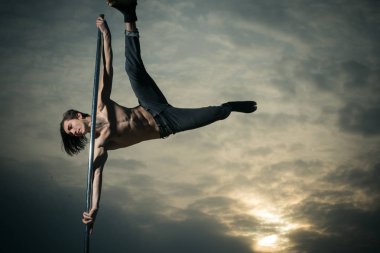 Gün batımı pilon üzerinde dans kas delikanlı. Pole dans spor. Güçlü adam dansçı egzersiz kutup. Seksi maço adam gökyüzü arka plan üzerinde uçmak. Atletik adam olun akrobatik öğeleri pilon üzerinde