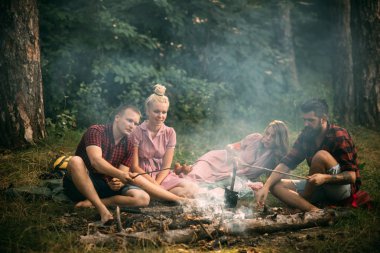 İki çiftler ormanda piknik. Sakallı adam ve ateşte sosis pişirme en iyi arkadaşı. Genç yürüyüşçü akşam kamp ateşi etrafında. Arkadaşlık ve eğlence kavramı
