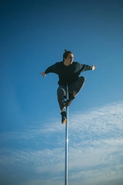 Atletische man maken acrobatische elementen op een pylon. Sexy macho man vliegen op blauwe hemelachtergrond. Jongeman dansen op pyloon. Sterke man danser training op paal. Pole dance sport. Opleiding tot de beste. — Stockfoto