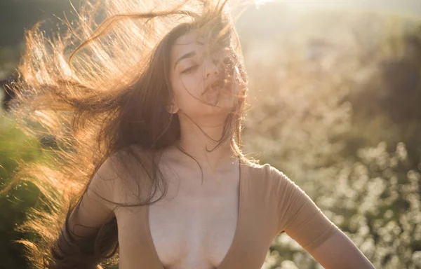 Kvinna på lugna ansikte njuta av solig och blåsig dag, naturen på bakgrund, oskärpa. Flicka med decollete njuta av håret vinka av vind. Damen ser attraktiva med viftande långt hår. Hair care koncept — Stockfoto