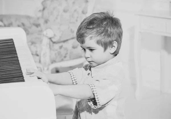 Educazione musicale. Bambino seduto vicino tastiera pianoforte, sfondo bianco. Il ragazzo passa il tempo libero vicino allo strumento musicale. Ragazzo carino e adorabile mette il dito sulla tastiera del pianoforte. Elite concetto di infanzia — Foto Stock