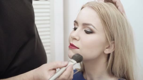 Maquillaje artista aplicar maquillaje a una atractiva mujer joven. Maquillaje para niña. Chica joven en el salón de belleza. Sexy rubia en salón de belleza — Vídeo de stock