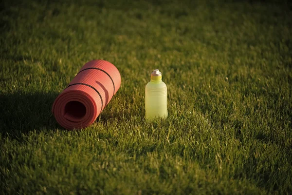 Equipamiento deportivo. Estera y botella de plástico en hierba verde, equipo de gimnasio — Foto de Stock