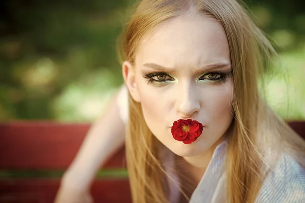 Hermosa modelo profesional manteniendo flor roja en la boca. Bella dama mirando directamente a la cámara . — Foto de Stock