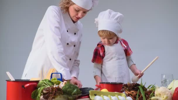 Mutlu bir çocukluk eğleniyor. Sevimli küçük çocuk ve mutfakta yemek yaparken gülümseyen güzel annesi. Genç aile yemek yemek mutfakta. Genç Anne ve oğlu birlikte yemek pişirme. — Stok video