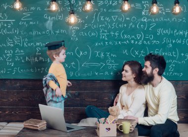 Evde eğitim kavramı. Lisansüstü şapkalı akıllı çocuk eğitim seviyor. Öğretim veliler evde çocuk. Çocuk Anne ve baba için onun bilgi sunma. Oğulları, kara tahta arka plan dinleme anne