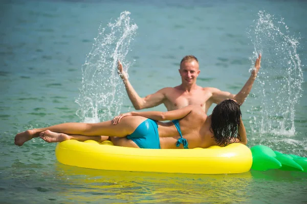 Sexy pareja feliz en el mar Caribe. Colchón inflable de piña, alegría de la actividad. Maldivas o agua de playa de Miami. Pareja en el amor baño de sol en la playa en el colchón de aire. Vacaciones de verano y viajes al océano — Foto de Stock